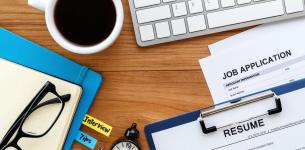 Image of a table containing a keyboard, job application, form, a CV, watch, spectacles and a cup of coffee.